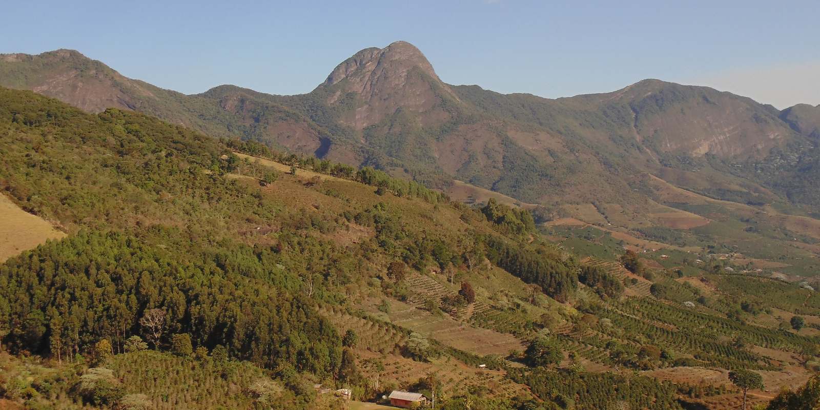 Serra do Caparaó vista de Dores do Rio Preto, com cafezais nas encostas e uma casa no meio do vale